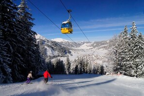 Een piste met een kabelbaan, sneeuwbedekte bomen en een skiër in een rode jas.