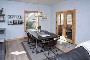 A dining area with a table, chairs, a hanging light fixture, a 'MARKET' sign, and a view through a glass door.