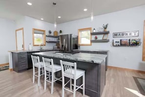 A modern kitchen with a large island, bar stools, and a refrigerator. - Waterfront Family Retreat on Green Bay w/ kayaks (Luxemburg)
