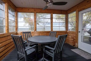 A wooden cabin with a round table and chairs, large windows, and a ceiling fan. - Waterfront Family Retreat on Green Bay w/ kayaks (Luxemburg)