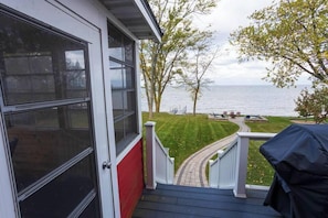 A view from a porch overlooking a body of water, with a lawn and a barbecue grill. - Waterfront Family Retreat on Green Bay w/ kayaks (Luxemburg)