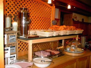 A buffet counter with various food items, a coffee machine, and a display case with baked goods. - Hotel Casada (Galtur)