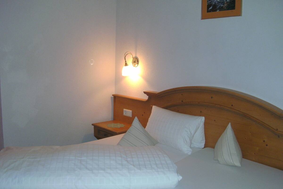 A neatly made bed with white bedding and pillows, a wooden headboard, and a nightstand with a lamp.