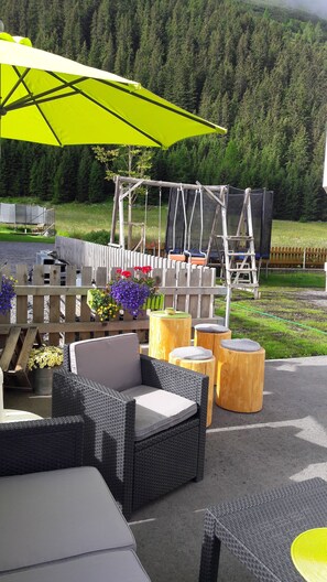 An outdoor seating area with wicker furniture, a yellow umbrella, and a wooden deck. - Hotel Casada (Galtur)