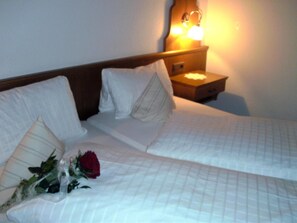 A neatly made bed with white linens and pillows, a wooden headboard, and a nightstand with a lamp. - Hotel Casada (Galtur)