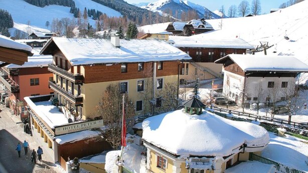 A snow-covered village with traditional buildings, a visible hotel named 'Hotel Peter,' and a mountain backdrop.