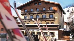 A multi-story building with a balcony on the second floor, a sign reading 'HOTEL PETER,' and a ski lift in the background.