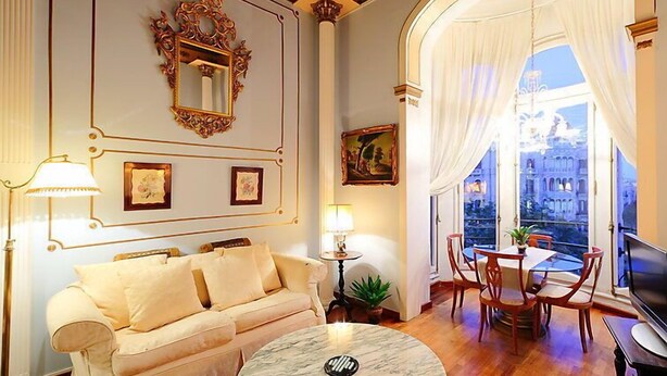 A living room with a sofa, a round marble coffee table, a TV, and a dining area with chairs and a table.