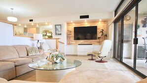 A modern living room with a sofa, a glass coffee table, and a TV mounted on a wooden wall.
