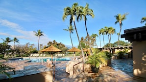 A pool area with lounge chairs, palm trees, and thatched umbrellas. - Family Vacation Home - Ocean Views - Walk to Beach - Sleeps 7 - Hosted by Owner (Lahaina)