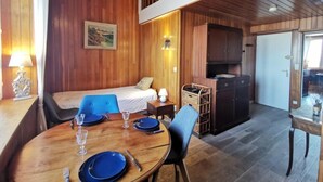 Ein gemütliches Blockhauszimmer mit Holzvertäfelung, einem Bett, einem Esstisch für zwei Personen und einer kleinen Küchenzeile.