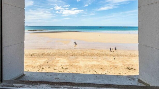 Blick auf einen Strand aus einem Fenster, strahlend blauer Himmel und ruhige See.