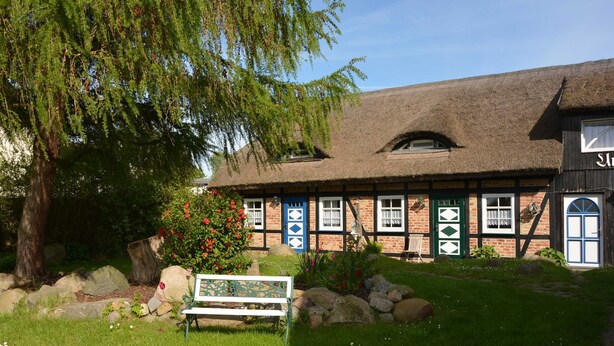 A traditional building with a thatched roof, a bench, and a garden with flowers and rocks. - E - Uns Schün, Germany (Middelhagen)