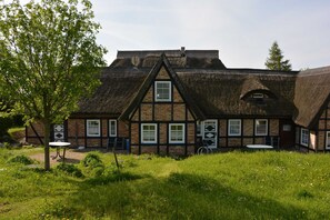 A traditional half-timbered house with a thatched roof, a small garden with a tree and a table, and a clear sky. - E - Uns Schün, Germany (Middelhagen)