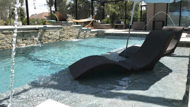 A pool area with a lounge chair, a stone wall, and a covered seating area. - Secret Escape (Rotonda West)