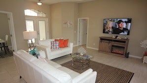 A living room with a white sofa, a glass coffee table, a fireplace, and a TV mounted on the wall. - Secret Escape (Rotonda West)