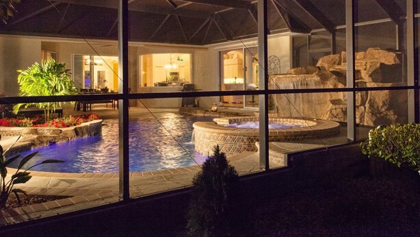 A pool area with a hot tub, a waterfall feature, and a view of the interior of a house through large windows. - Amazing Lagoon (Rotonda West)
