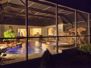 Et poolområde med jacuzzi, et vandfald og udsigt til husets indre gennem store vinduer.