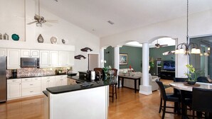 A spacious kitchen with a central island, white cabinetry, and a microwave. There is a dining area with a table and chairs, and a living room with a television. - Amazing Lagoon (Rotonda West)