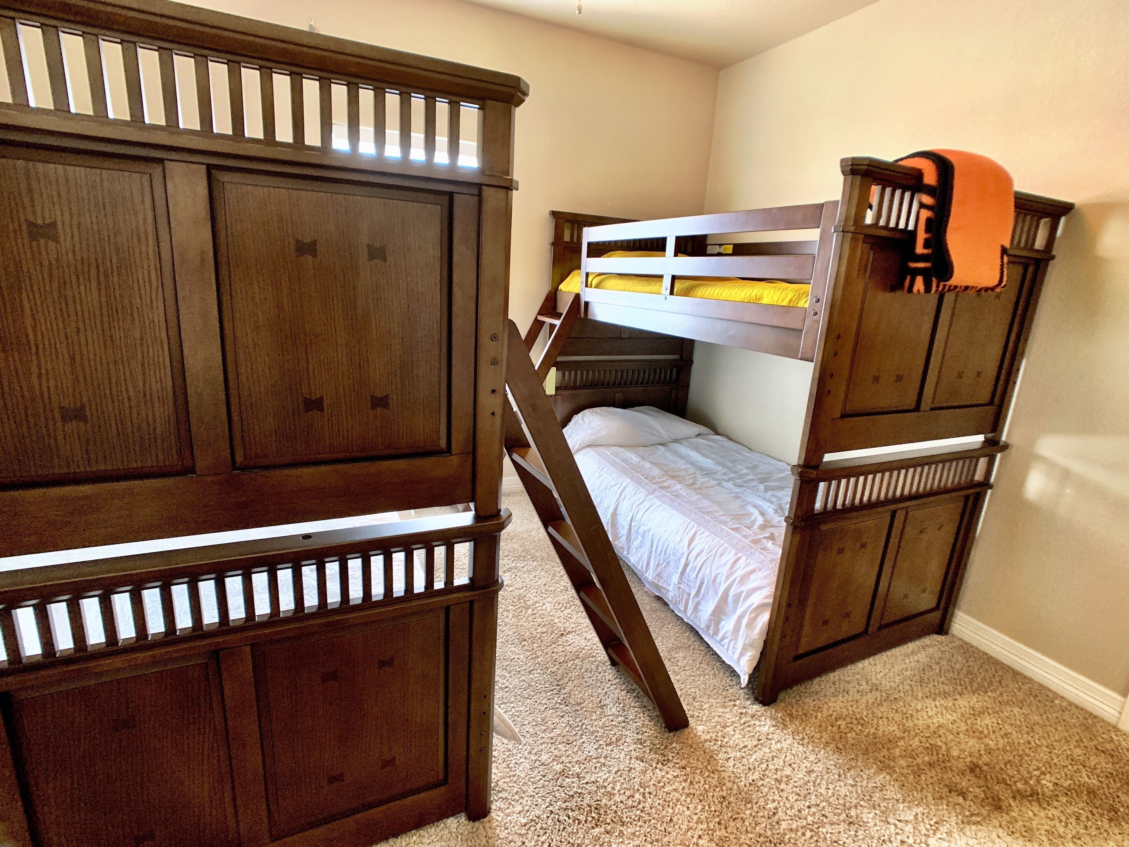 A bunk bed with a wooden headboard and footboard, a small desk, and a carpeted floor.