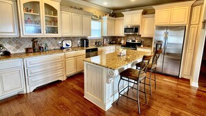 A spacious kitchen with white cabinetry, a granite countertop, a central island with bar stools, a stainless steel refrigerator, and a ceiling fan. - LOS PELICANOS - 2 bedroom, Gulf View, Palapa Bar on deck!! (Crystal Beach)