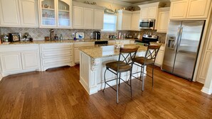 A spacious kitchen with white cabinetry, a central island with bar stools, a stainless steel refrigerator, and a ceiling fan. - LOS PELICANOS - 2 bedroom, Gulf View, Palapa Bar on deck!! (Crystal Beach)