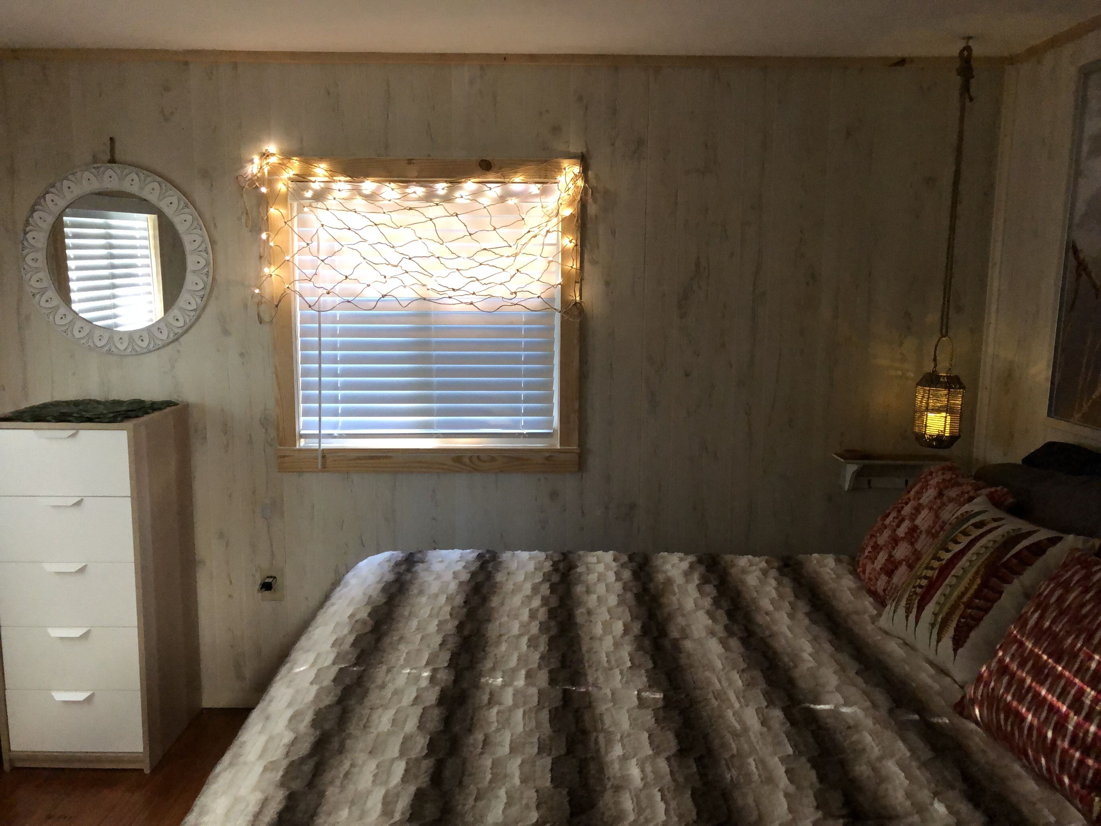 Un dormitorio con cama, cómoda, ventana con persianas y una lámpara colgante.