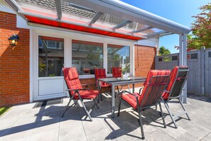 A patio with a table and chairs, a glass door, and a brick wall. - Apartment "below" - "House Passat" (Neuharlingersiel)