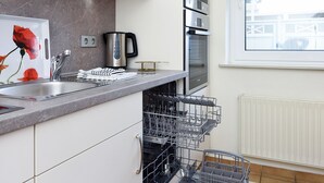 A modern kitchen with white cabinets, stainless steel appliances, and a dishwasher. - Apartment "below" - "House Passat" (Neuharlingersiel)