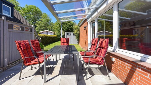 A covered patio with a table and chairs, a glass enclosure, and a brick wall. - Apartment "below" - "House Passat" (Neuharlingersiel)