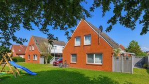 A residential area with a brick house, a blue slide, and a car parked in the driveway. - Apartment "below" - "House Passat" (Neuharlingersiel)
