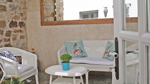 A cozy patio area with wicker furniture, a tiled floor, and a stone wall. - Evreka Butik Otel (Bozcaada)