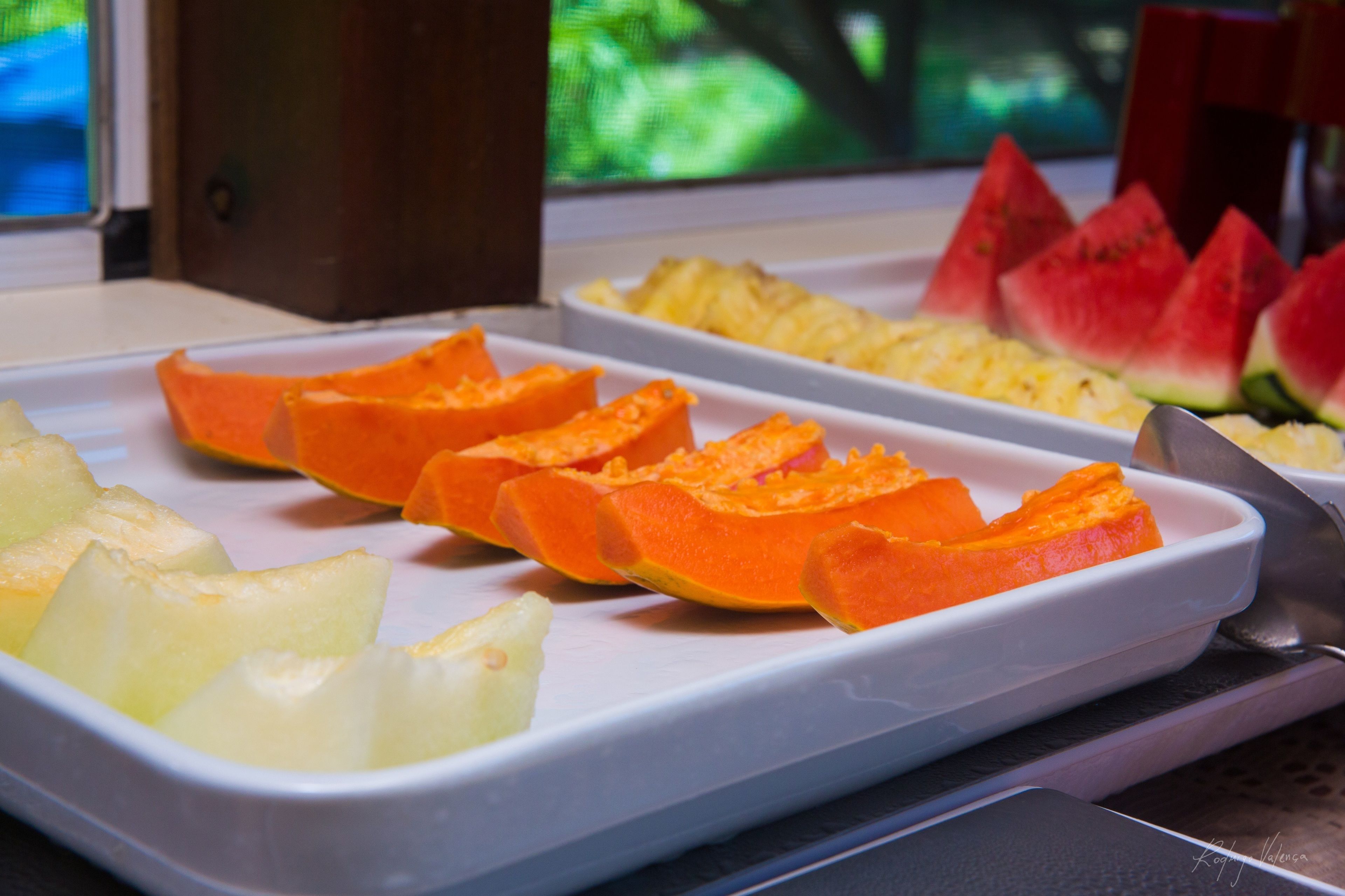 Een schaal met plakjes fruit, waaronder ananas en papaja, op een wit bord.