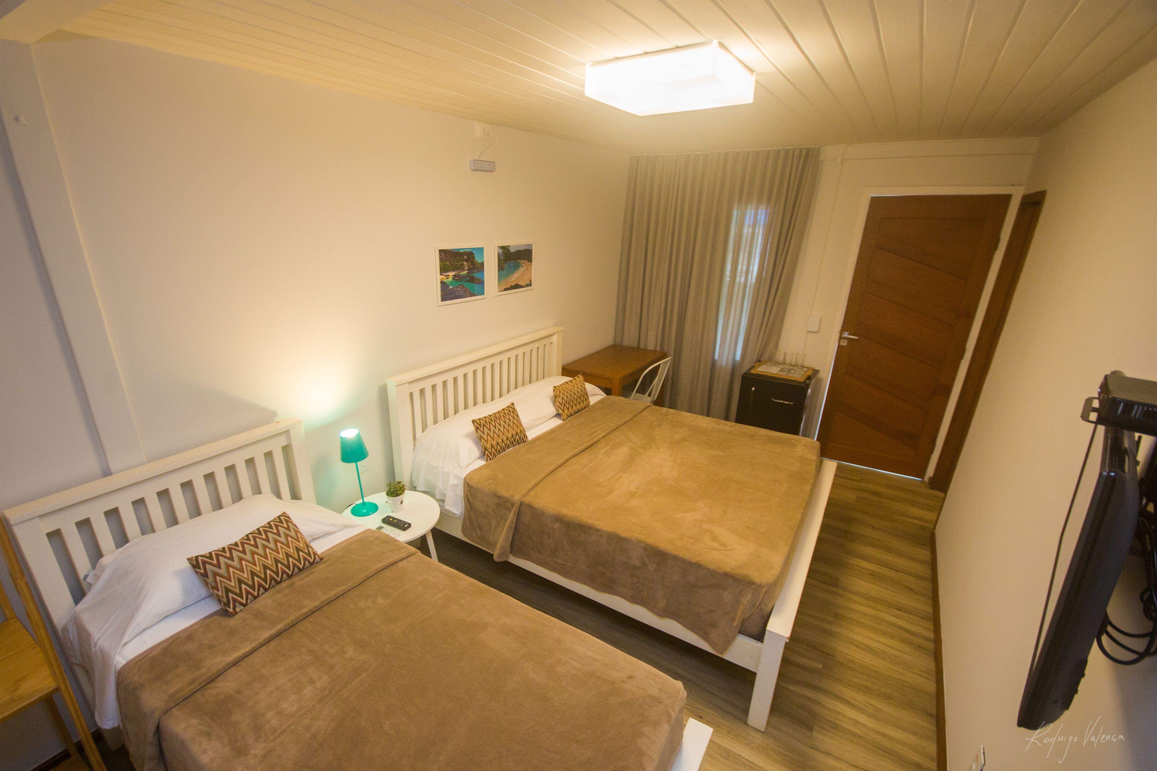 A hotel room with two beds, a small table with a lamp, a door, and a television.