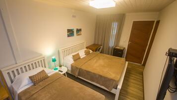 A hotel room with two beds, a small table with a lamp, a door, and a television.