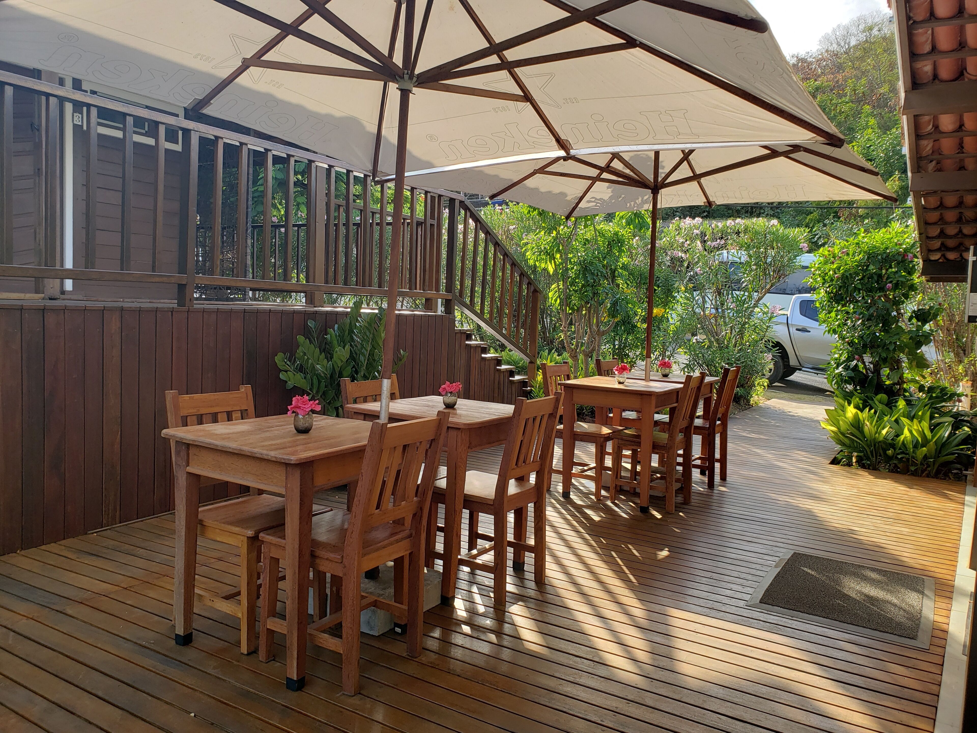 Une terrasse extérieure avec des tables et des chaises en bois, protégée par de grands parasols et entourée de verdure.