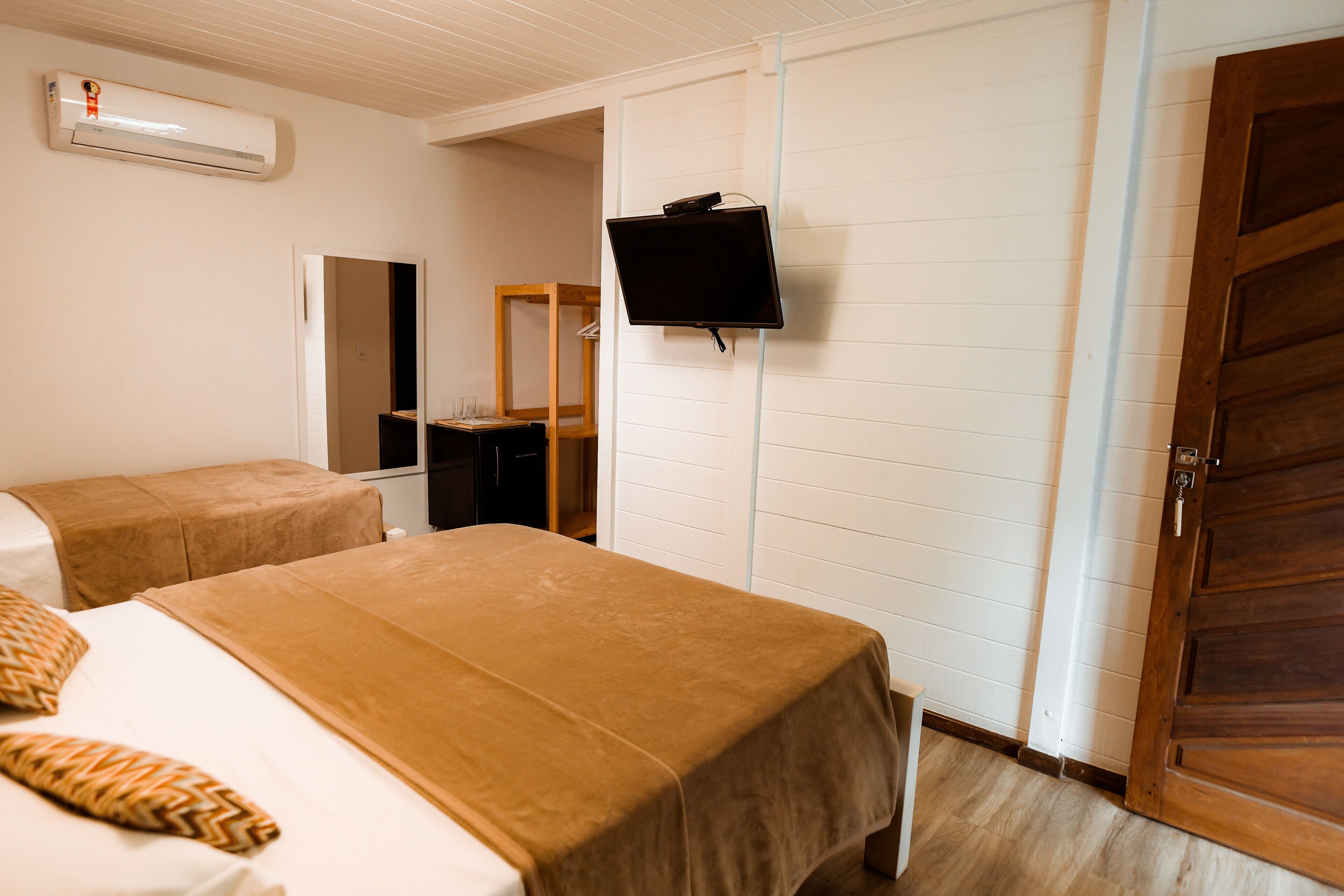 Habitación de hotel con dos camas, un televisor montado en la pared, una puerta de madera y un armario.