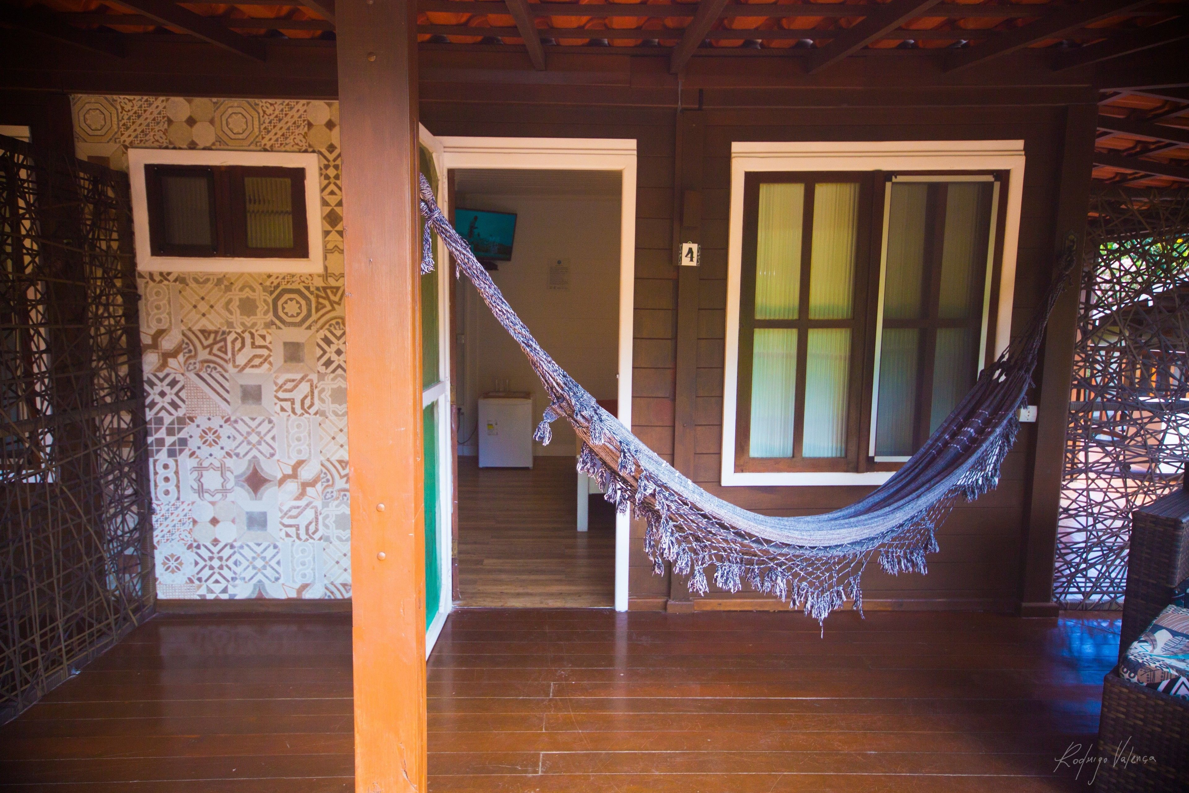 Una hamaca en una habitación con suelo de madera, paredes con diseños y una puerta que da a otra habitación.
