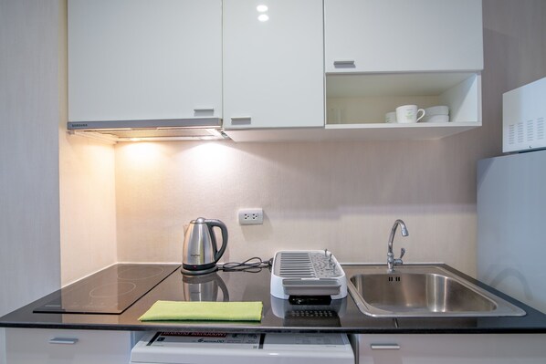 A compact kitchen with a built-in dishwasher, a kettle, a coffee maker, and a sink.