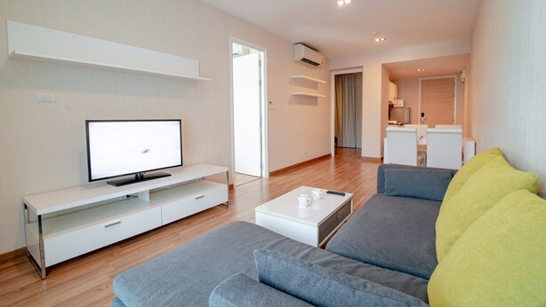 A modern living room with a flat-screen TV, a white coffee table, and a gray sofa. - My Resort Beach Apartment 2 (Tambon Nong Kae)