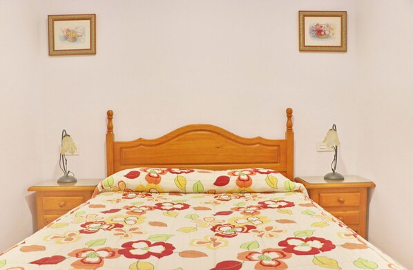 A bed with a floral bedspread, wooden headboard, two bedside lamps, and a nightstand with a drawer.