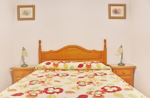 A bed with a floral bedspread, wooden headboard, two bedside lamps, and a nightstand with a drawer.