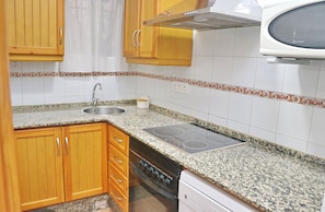 A kitchen with wooden cabinets, a granite countertop, a stainless steel sink, a stove, and a microwave.