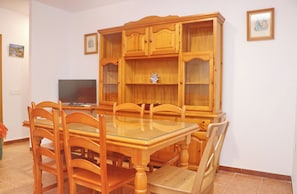 A dining area with a glass-top table, wooden chairs, and a wooden cabinet with glass doors.