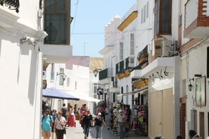 A narrow street with white buildings, some shops, and pedestrians.