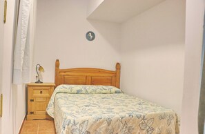 Une chambre à coucher avec un lit en bois, une table de chevet avec une lampe, un rideau à carreaux et une horloge murale.