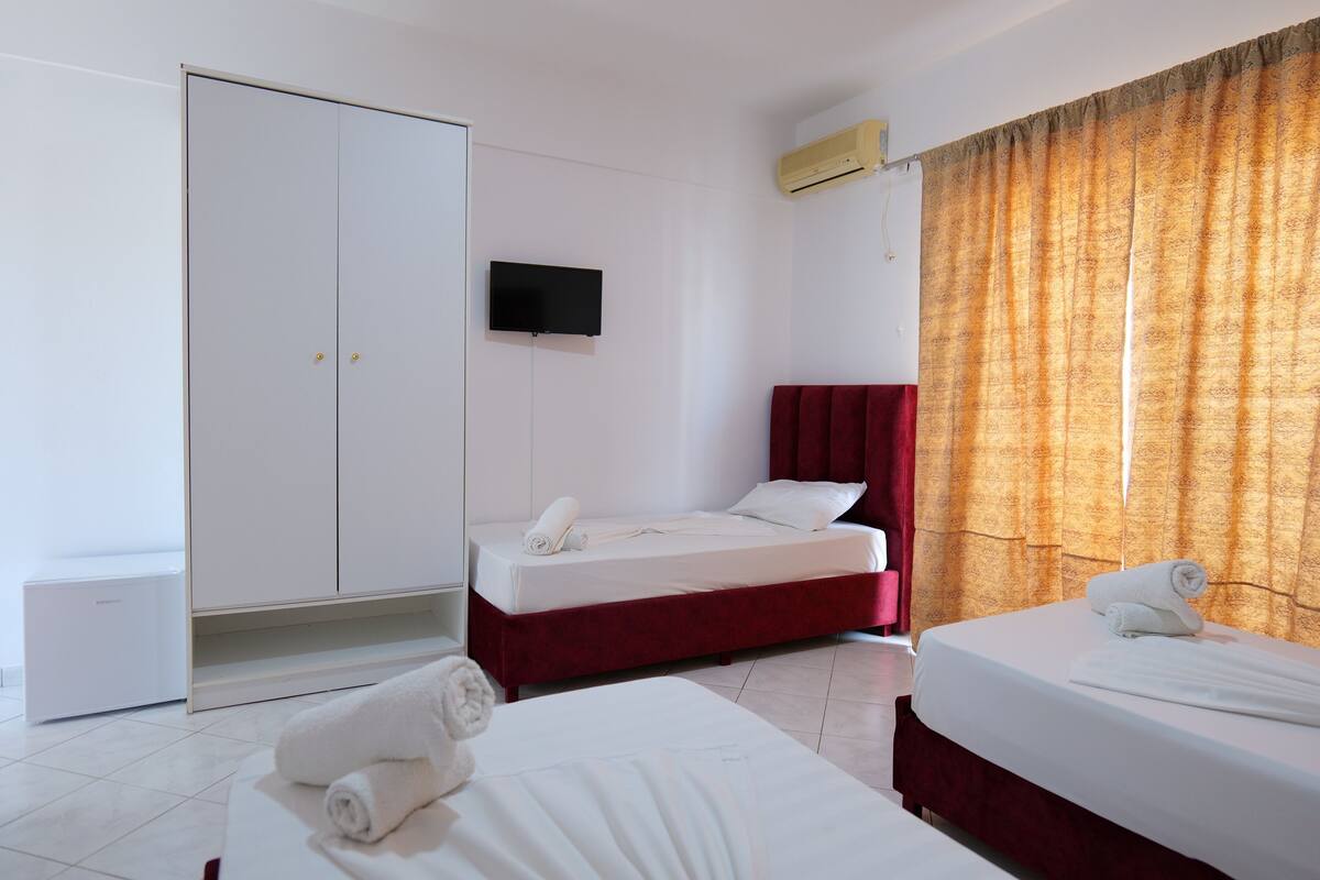 Habitación de hotel con cama, armario, televisión y ventana con cortinas.
