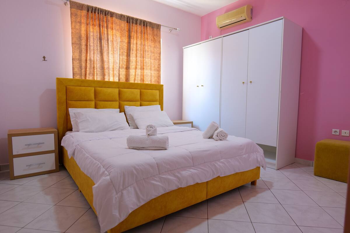 Un dormitorio con cama, armario, mesita de noche y ventana con cortinas.