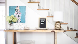A wooden console table with a framed welcome sign, a vase of flowers, and a decorative lamp. - Historic Cottage in the Heart of the Village (Granville)