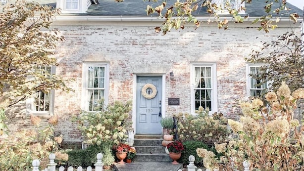A two-story stone house with a white picket fence, a front door with a wreath, and a number "120" on the door. - Historic Cottage in the Heart of the Village (Granville)